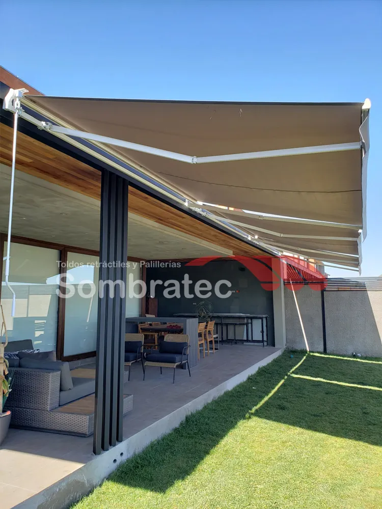 Toldo retráctil beige extendido sobre un patio con césped y ventanal