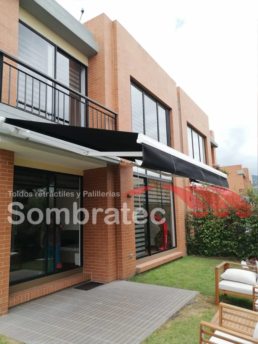 Toldo retráctil negro instalado sobre la ventana de una casa de dos pisos